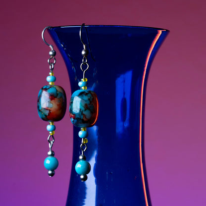 Aurora drop earrings hanging on a blue base.